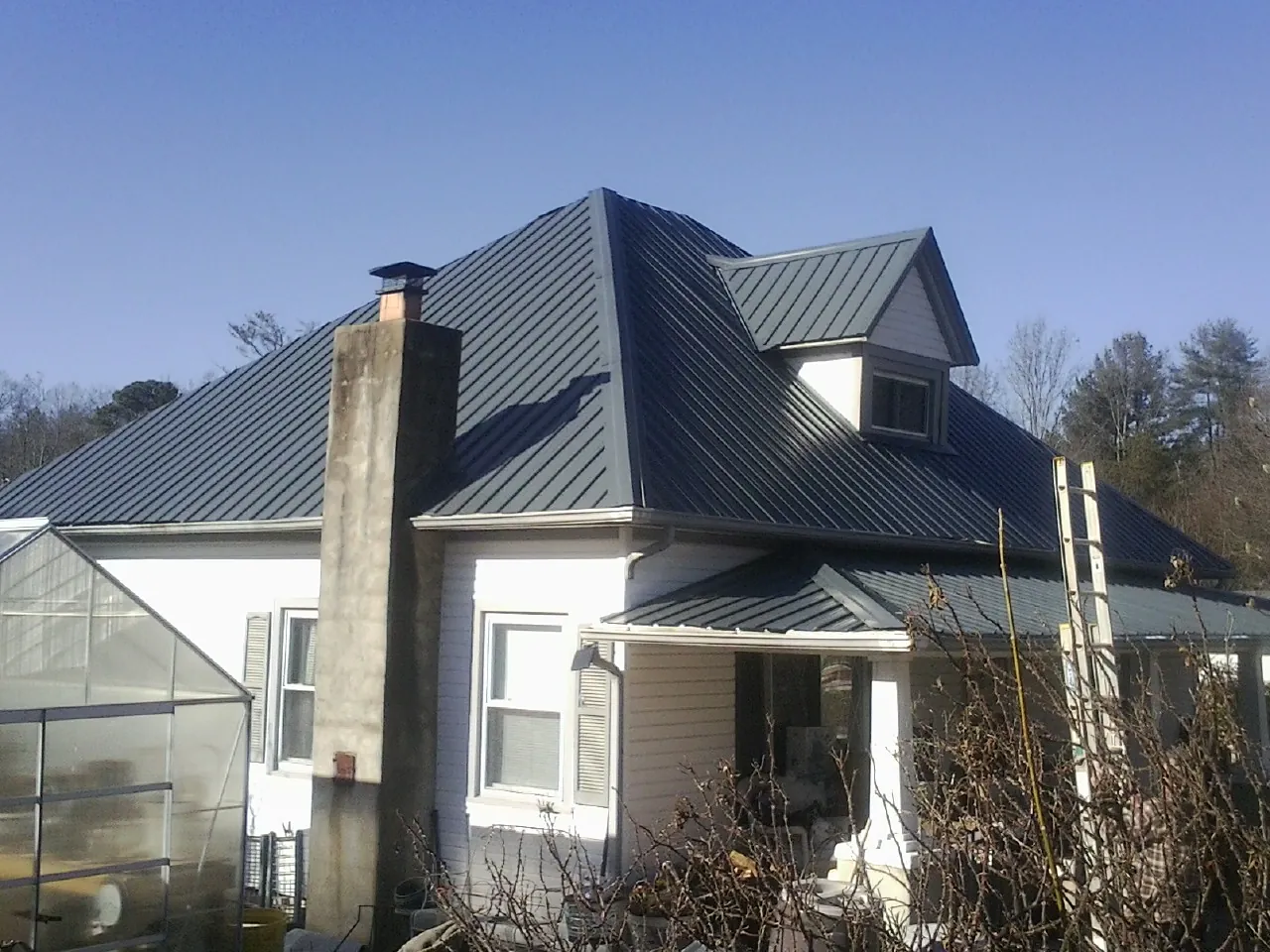 Dark blue standing seam metal roof on a white farmhouse with dormer — Slate & Tile Roof Repair by Roofing Brothers in Molt
