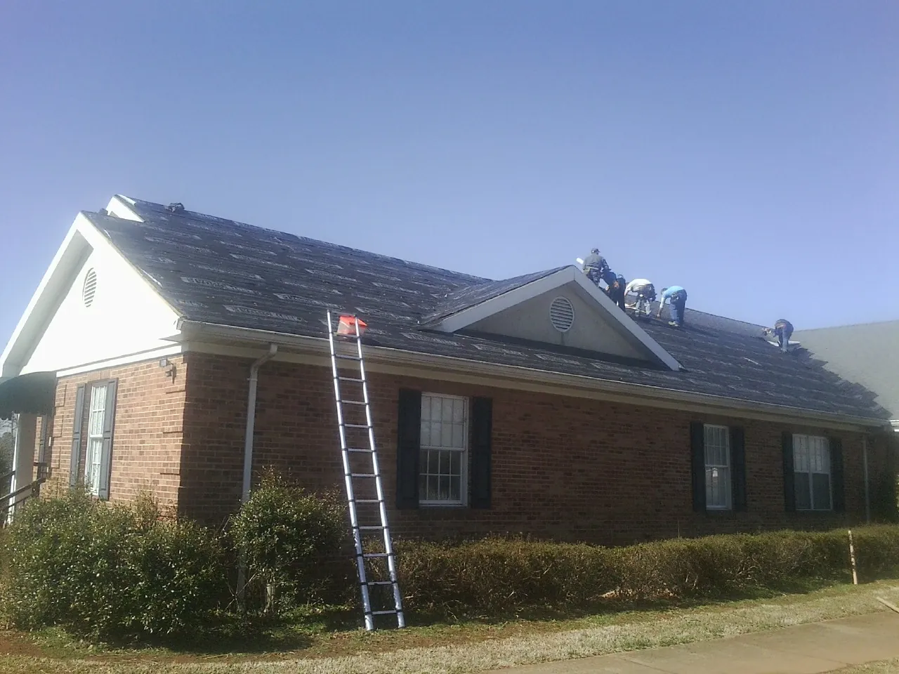 Crew tearing shingles off a brick ranch roof with a ladder set — Emergency Roof Repair work by our crew in Molt