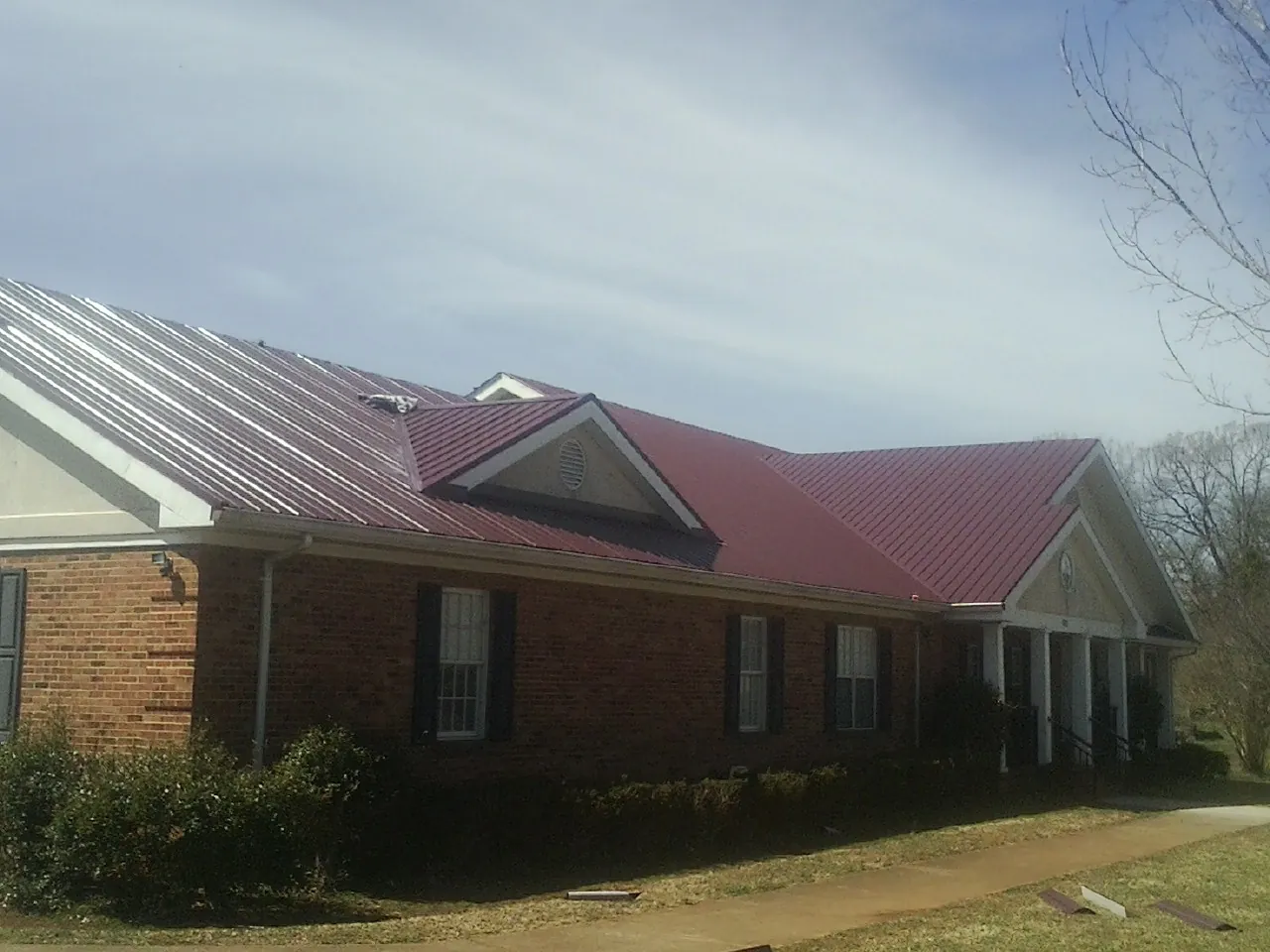 Red metal roof with gabled entries on a long brick building, from a Hail Damage Roof Repair job in Molt