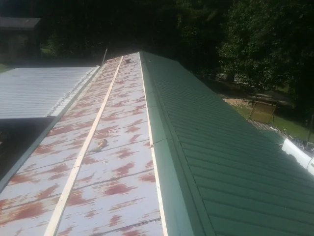 Old rusted panels beside newly installed green metal roofing — Wind Damage Roof Repair by Roofing Brothers in Molt