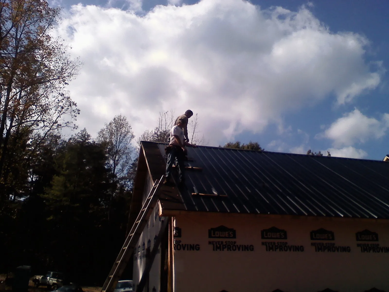 Roofer fastening dark metal panels high against a cloudy sky, from a Roof Inspection job in Molt