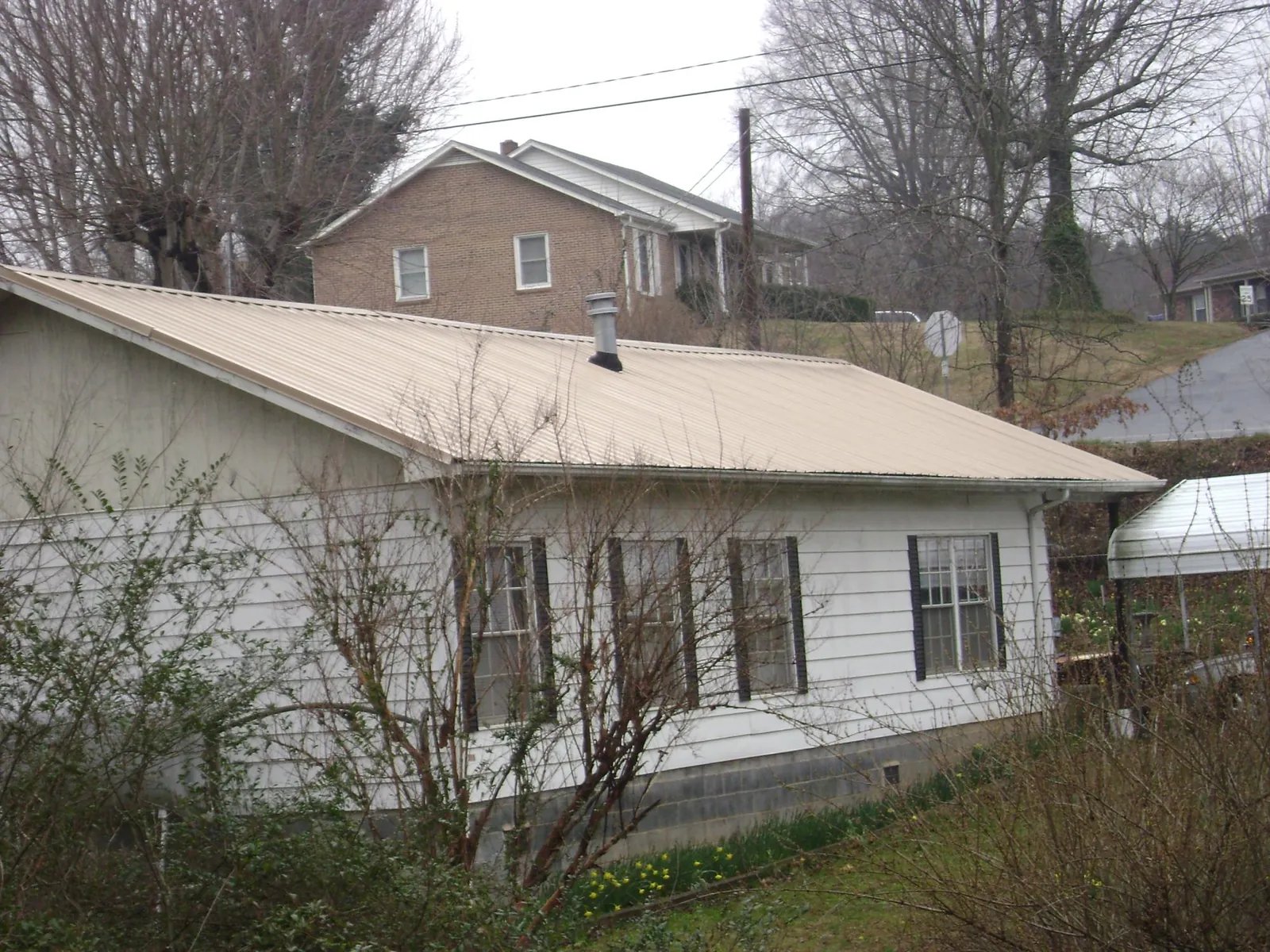 Tan metal roof on a white sided house set into a hillside — Commercial Roofing by Roofing Brothers in Molt