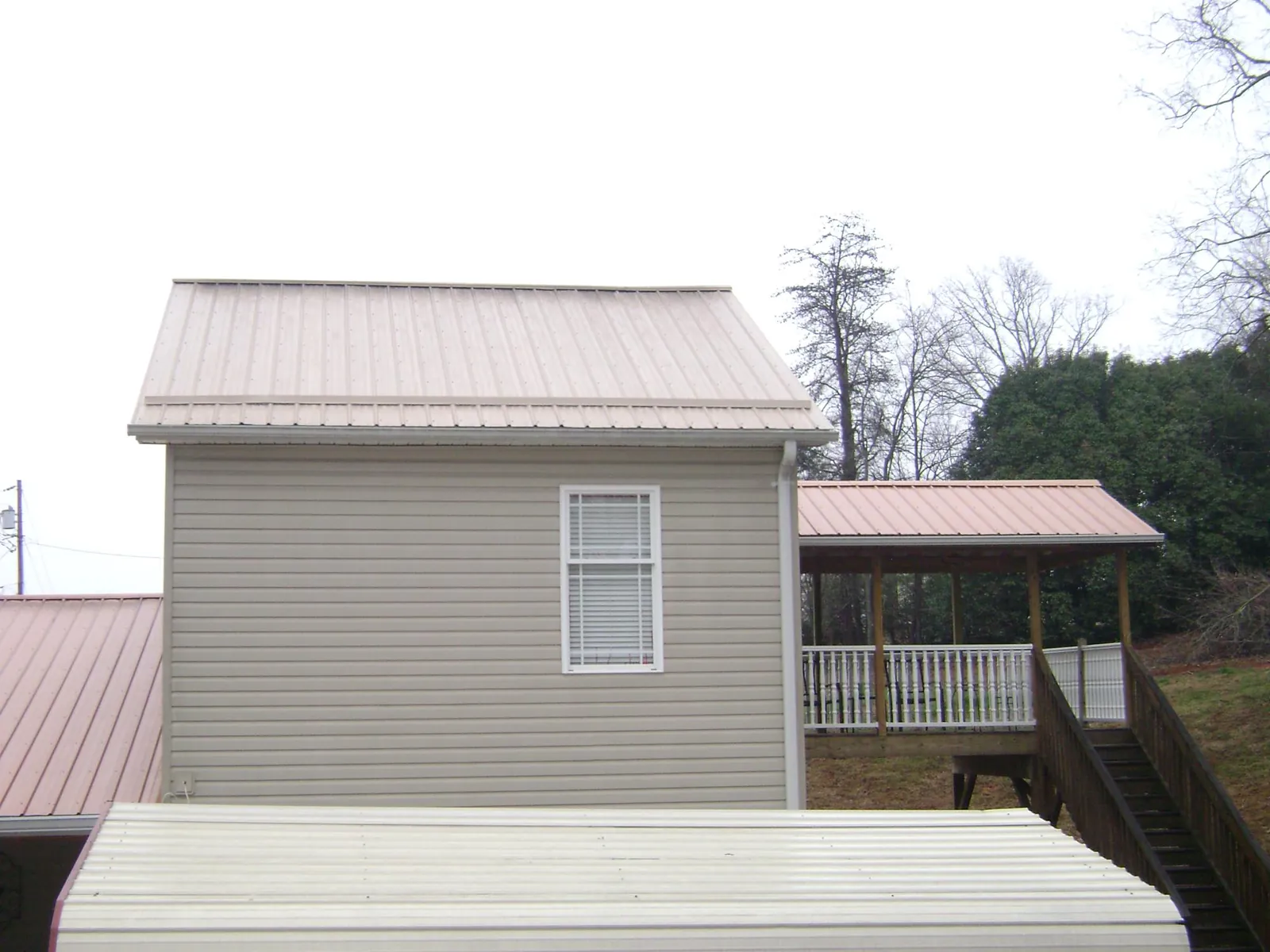 Tan metal roofs on a two story addition and attached porch, from a Roof Replacement job in Molt